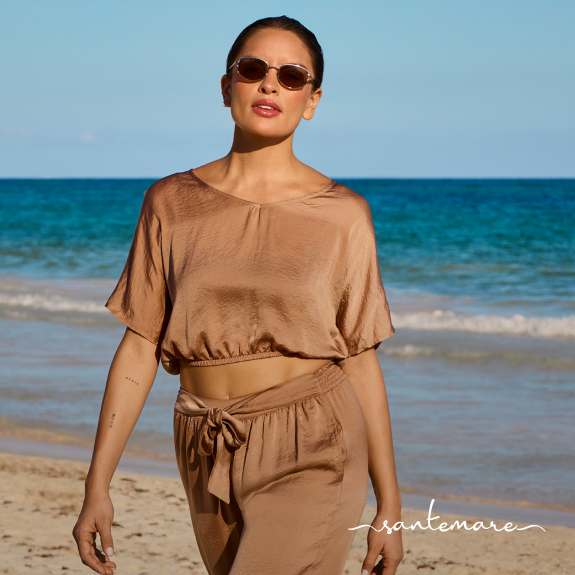 Femme marchant sur la plage et portant un ensemble coordonn&eacute; d&rsquo;un haut et pantalon en satin beige de la marque Santemare. 